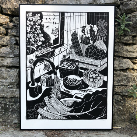cadre en alu posé sur un muret de pierre représentant une linogravure en noir et blanc d'une scène de retour de marché, avec des légumes de saison dans une cagette en bois, blettes fraises petits pois asperges, on voit des hirondelles par la fenetre.